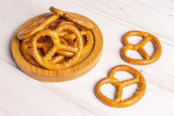 Lot of whole salty brown pretzel on bamboo coaster on white wood