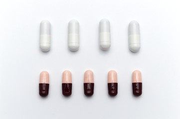 Prescription drugs, capsules of different colors between white capsules and dark reddish brown and soft pink all mix in . On white background.