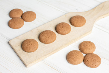 Group of ten whole sweet brown chocolate sponge biscuit on small wooden cutting board on white wood