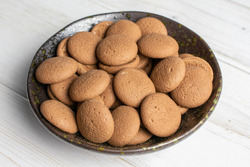 Lot of whole sweet brown chocolate sponge biscuit in dark ceramic bowl on white wood