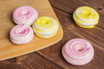 Group of five whole pink and yellow sweet meringue on bamboo cutting board on brown wood