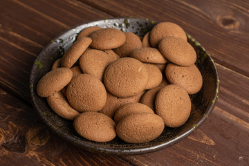 Lot of whole sweet brown chocolate sponge biscuit in dark ceramic bowl on brown wood