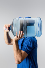 Side view of courier carrying on shoulder bottled water isolated on grey