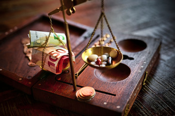 An old scale with money on one side and tablets on the other as a symbol of healthcare costs. The focus lies on the banknotes.