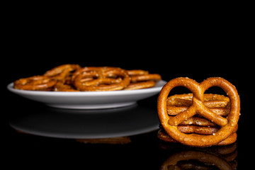 Lot of whole salty brown pretzel on white ceramic plate isolated on black glass