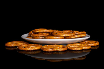 Lot of whole salty brown pretzel on white ceramic plate isolated on black glass