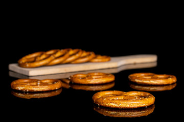 Group of nine whole salty brown pretzel on small wooden cutting board isolated on black glass
