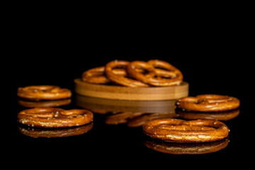 Lot of whole salty brown pretzel on bamboo coaster isolated on black glass
