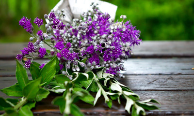 Bouquet of purple wildflowers wrapped in newspaper on rustic wooden table