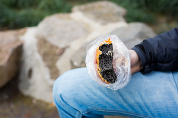A bitten piece of black colored bread in a male hand. Black colored bun inside. Fast food. Coal Bread. Chinese food