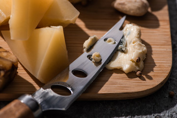 Selective focus of soft dorblu pressed by knife next to pieces of grana padano on cutting board