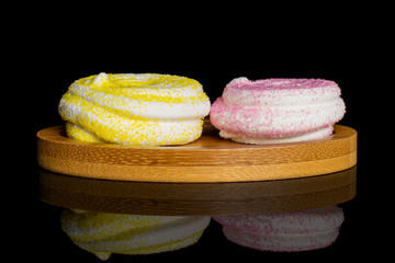 Obraz na płótnie Canvas Group of two whole pink and yellow sweet meringue on bamboo coaster isolated on black glass