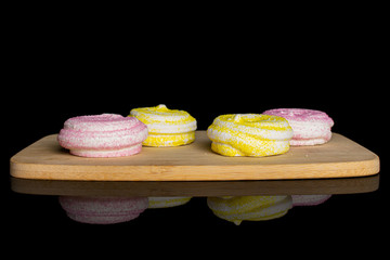 Group of four whole pink and yellow sweet meringue on bamboo cutting board isolated on black glass