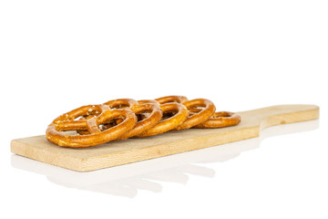 Group of five whole salty brown pretzel on small wooden cutting board isolated on white background