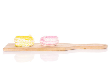 Group of two whole pink and yellow sweet meringue on small wooden cutting board isolated on white background