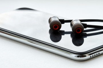 Black earphones lie on the modern smartphone. White background, closeup