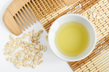 Small white bowl with olive (or coconut) oil, oatmeal and wooden hair comb. Homemade skin and hair treatment concept. Top view, copy space 