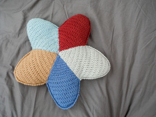 Closeup hand made multicolored yarn knitted pillow in the shape of a starfish on a gray background. Natural materials for the interior. Chemical free textile