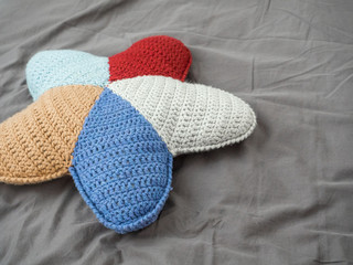 Closeup hand made multicolored yarn knitted pillow in the shape of a starfish on a gray background. Natural materials for the interior. Chemical free textile