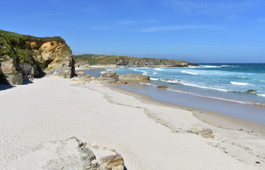 Fototapeta na wymiar Beach with white sand, cliff and waves breaking on a sunny day. Viveiro, Lugo, Galicia, Spain.