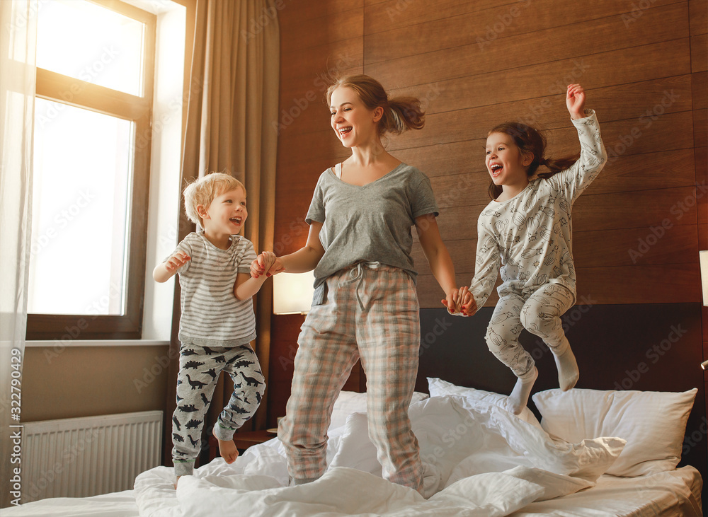 Wall mural happy family mother and children son and daughter jumping, laughing, playing in bed.