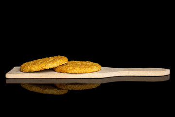 Group of two whole sweet golden oat cookie on small wooden cutting board isolated on black glass