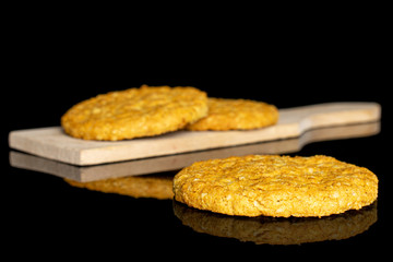 Group of three whole sweet golden oat cookie on small wooden cutting board isolated on black glass