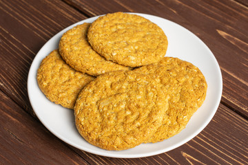 Group of six whole sweet golden oat cookie on white ceramic plate on brown wood