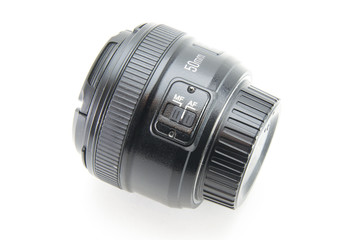 A black lens with 50mm covers with a 1.8 aperture lies on its side on a white isolated background