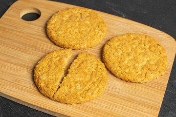 Group of two whole two halves of sweet golden oat cookie on bamboo cutting board on grey stone
