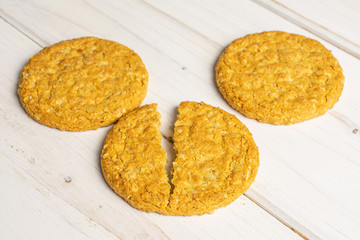 Group of two whole two halves of sweet golden oat cookie on white wood