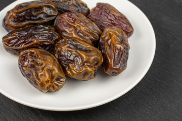 Lot of whole dry brown date fruit on white ceramic plate on grey stone