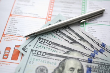 The silver pen with dollar banknotes is on the international euro-protocol form for filling and indemnification as a result of a traffic accident without police participation concept.