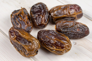 Group of six whole dry brown date fruit on white wood