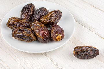 Group of eight whole dry brown date fruit on white ceramic plate on white wood