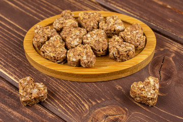 Lot of whole healthy brown cereal heart with cocoa on bamboo coaster on brown wood