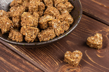 Lot of whole healthy brown cereal heart with cocoa in dark ceramic bowl on brown wood