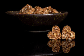 Lot of whole healthy brown cereal heart with cocoa in dark ceramic bowl isolated on black glass