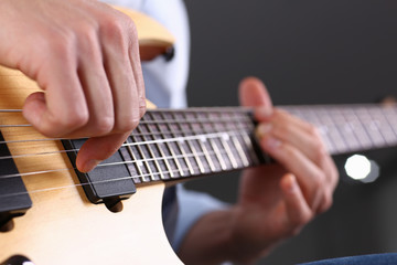Male arms holding and playing classic shape wooden electric guitar closeup. Six stringed learning...