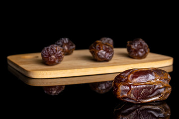 Group of six whole dry brown date fruit on bamboo cutting board isolated on black glass