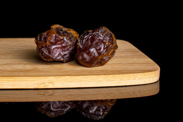 Group of two whole dry brown date fruit on bamboo cutting board isolated on black glass