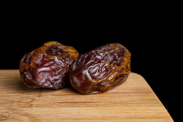 Group of two whole dry brown date fruit on bamboo cutting board isolated on black glass