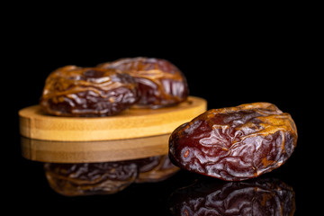 Group of three whole dry brown date fruit on bamboo coaster isolated on black glass