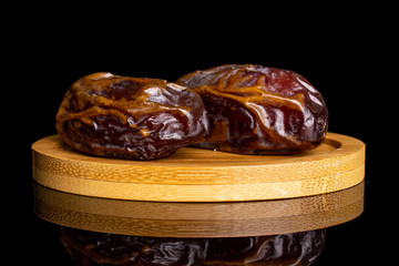 Group of two whole dry brown date fruit on bamboo coaster isolated on black glass