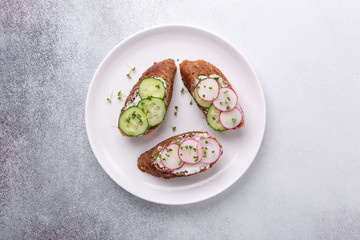 Healthy sandwiches with grain bread, ricotta, cucumber, radish and mustard micro greens. On white plate, top view. Healthy snack