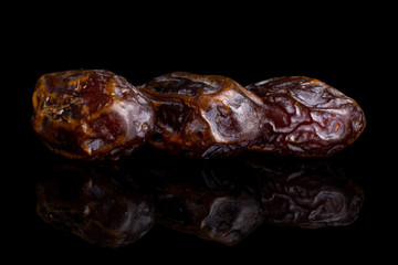 Group of three whole dry brown date fruit in row isolated on black glass