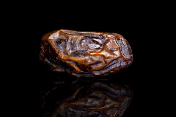 One whole dry brown date fruit isolated on black glass