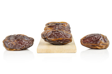 Group of five whole dry brown date fruit on small wooden cutting board isolated on white background
