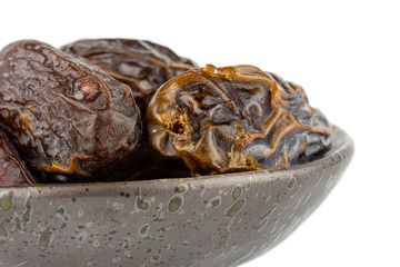 Group of three whole dry brown date fruit in dark ceramic bowl isolated on white background