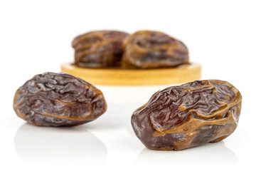 Group of four whole dry brown date fruit on bamboo coaster isolated on white background